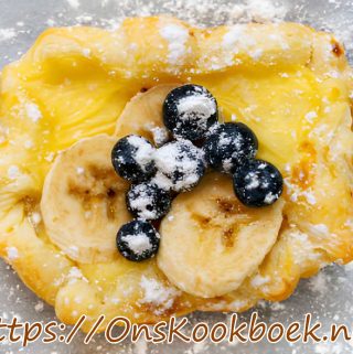 Bananentaart met bladerdeeg en vanillepudding, afgewerkt met verse banaan, blauwe bessen en poedersuiker